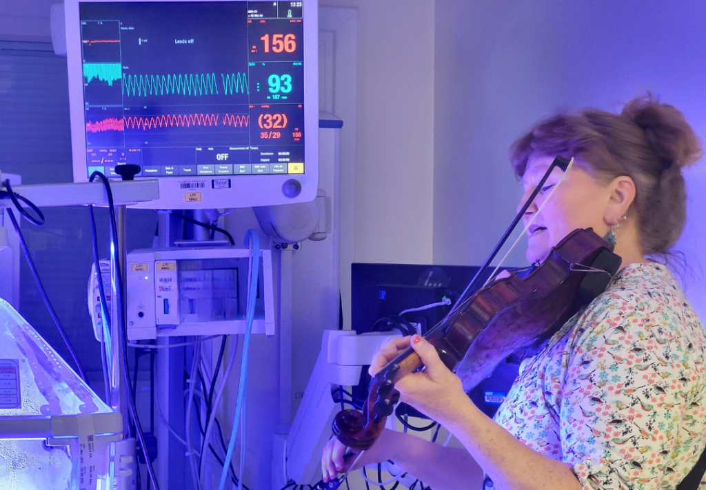 A photo of Sarah playing violin to a baby in NICU
