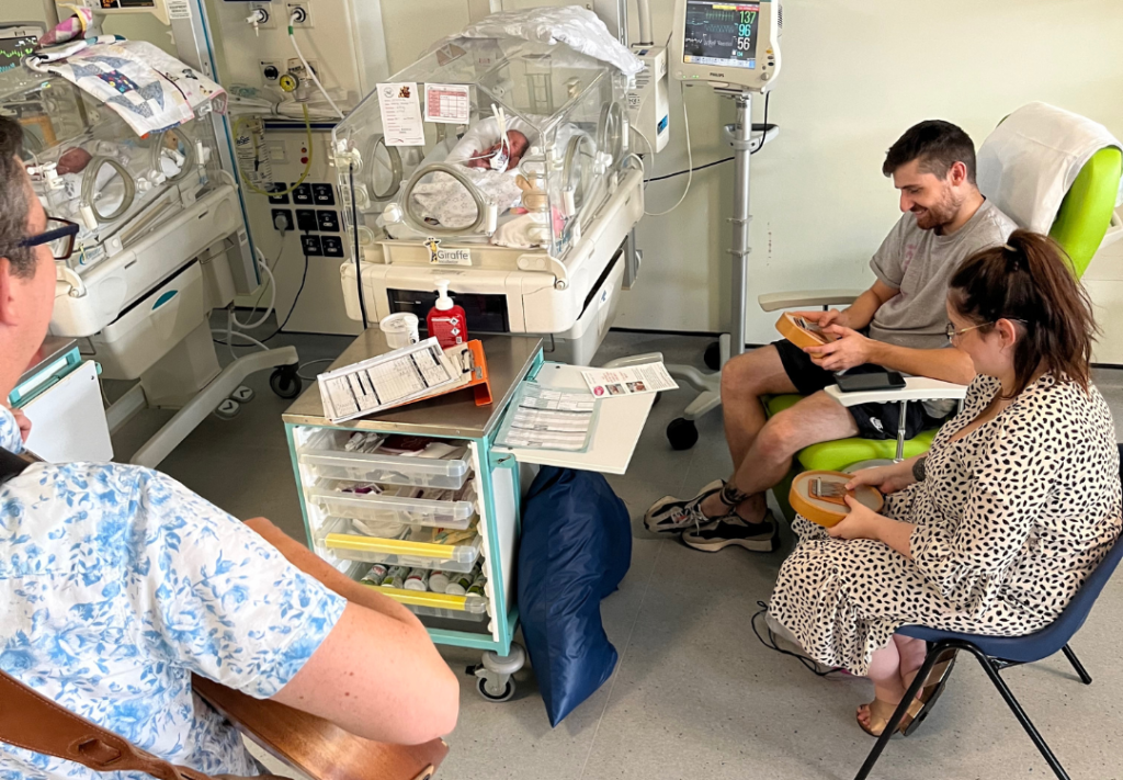 A photo of Nick and two parents playing to two babies in NICU